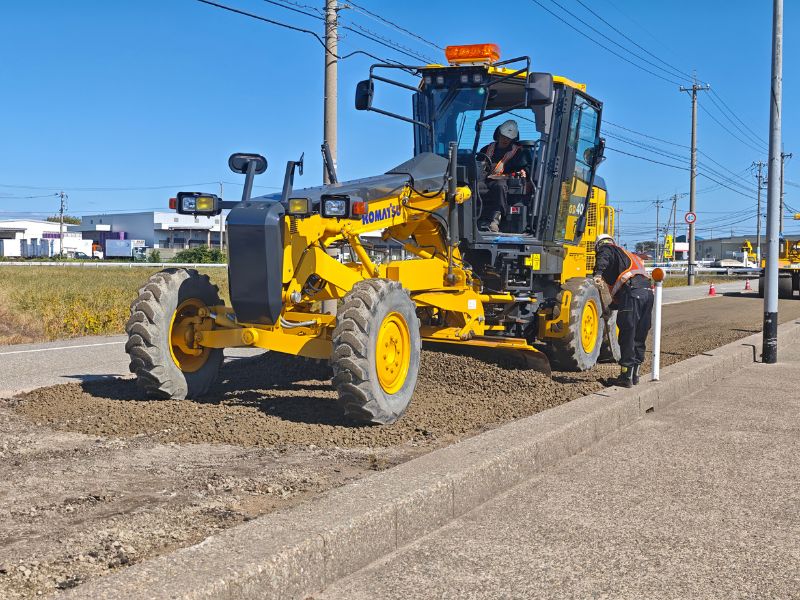 ロードワークスの最新式のモーターグレーダーが路盤を整正している様子